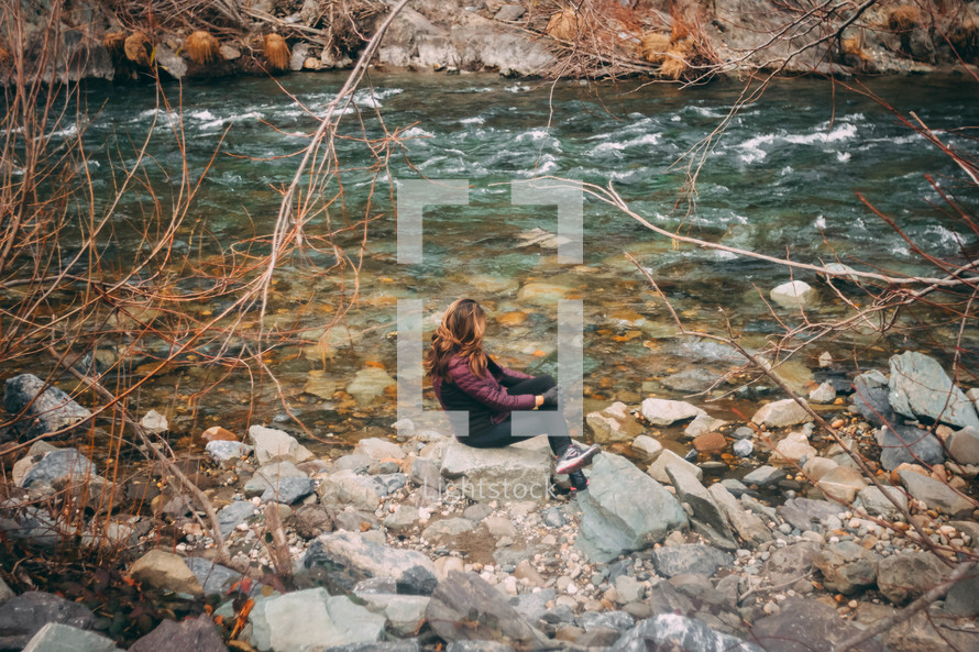 woman sitting on rocks along a riverbank 