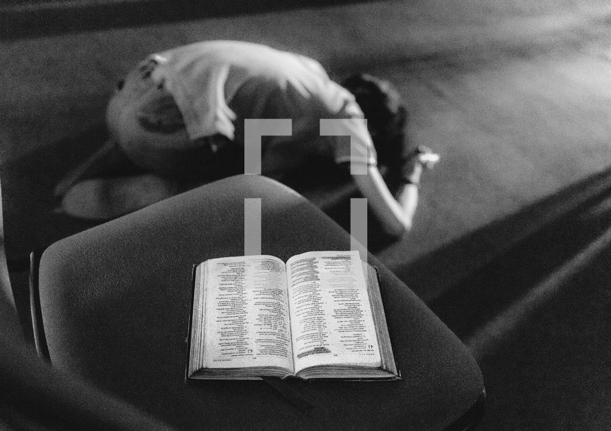 kneeling in prayer with a Bible in a chair 