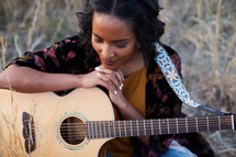 a woman sitting in a field with a guitar praying 