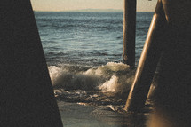 waves crashing into posts from a pier 