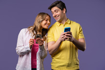 Young couple using mobile device. Woman and man watching, talking, smiling, laughing with smartphone. Social apps, networks, technology concept. Violet studio background.