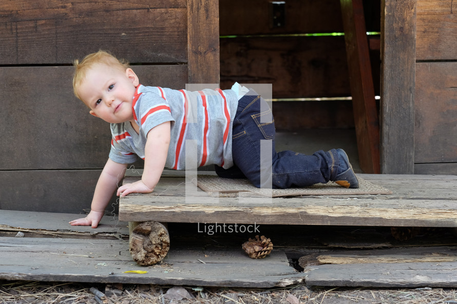 A baby boy crawling on a rustic wood porch.