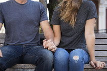 torso of a couple sitting on a bench holding hands 