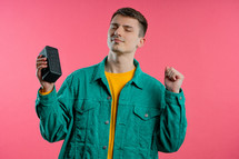 Man dancing, enjoying on yellow studio background. Guy moves to rhythm of music. Young teenager listening to music by wireless portable speaker - modern sound system. High quality