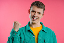 Handsome man shows triumph yes YEAH gesture of victory, he achieved result, goals. Guy glad, happy, surprised excited happy lady on pink background. Jackpot concept. High quality