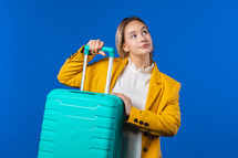 Young pretty woman with carry-on suitcase on blue background. Teenager traveling with blue luggage bag for airplane hand baggage. Summer travel, vacation concept. High quality photo