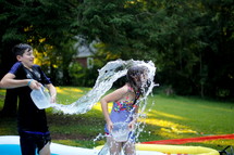 a brother splashing his sister with a bucket of water