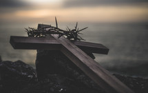 wooden cross and crown of thorns on a rock at sunset 