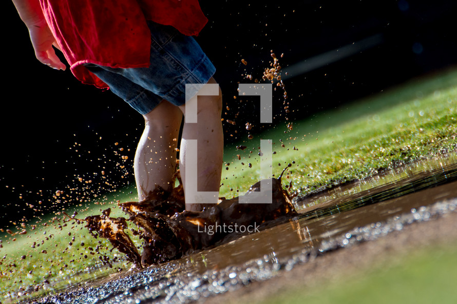 Child splashing in a mud puddle.
