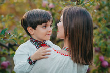 Tender scene of loving son with mom on apple orchard backdrop with sunlight. Beautiful family. Cute 4 years old kid with mother. Parenthood, childhood, happiness, children wellbeing concept.