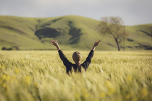 a woman standing in a field of wheat with raised hands 