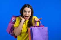 Excited woman with colorful paper bags after shopping on blue studio background. Concept of seasonal sale, purchases, spending money on gifts. High quality photo
