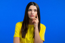 Thinking woman looking up on blue studio background. Pensive face expressions. Pretty model with attractive appearance . High quality photo