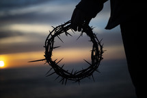 man holding a crown of thorns at sunset 