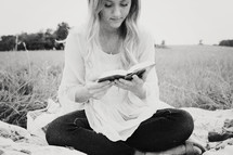 woman sitting on a blanket in the grass reading a book 