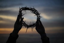 silhouette of a man holding up a crown of thorns at sunset 