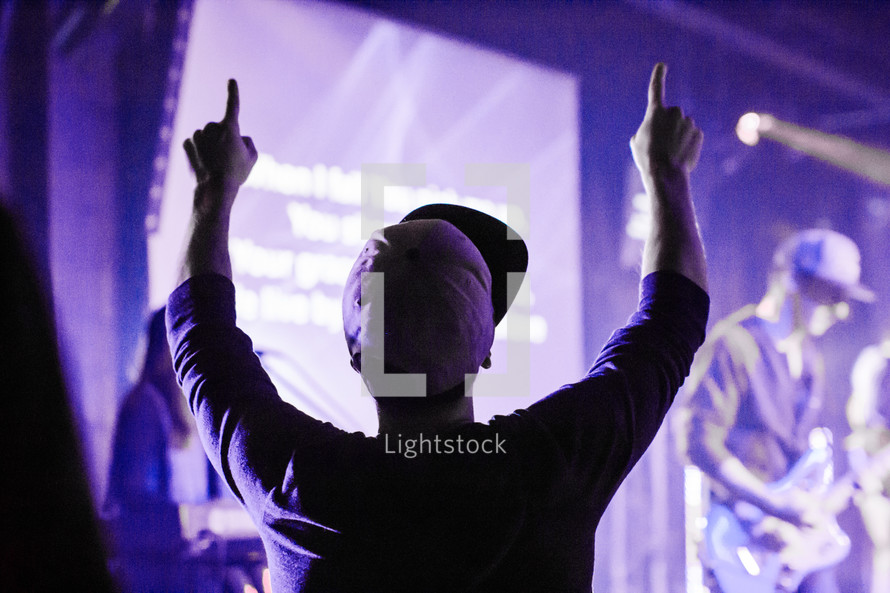 Boy in baseball cap at a concert with his fingers pointed in the air.