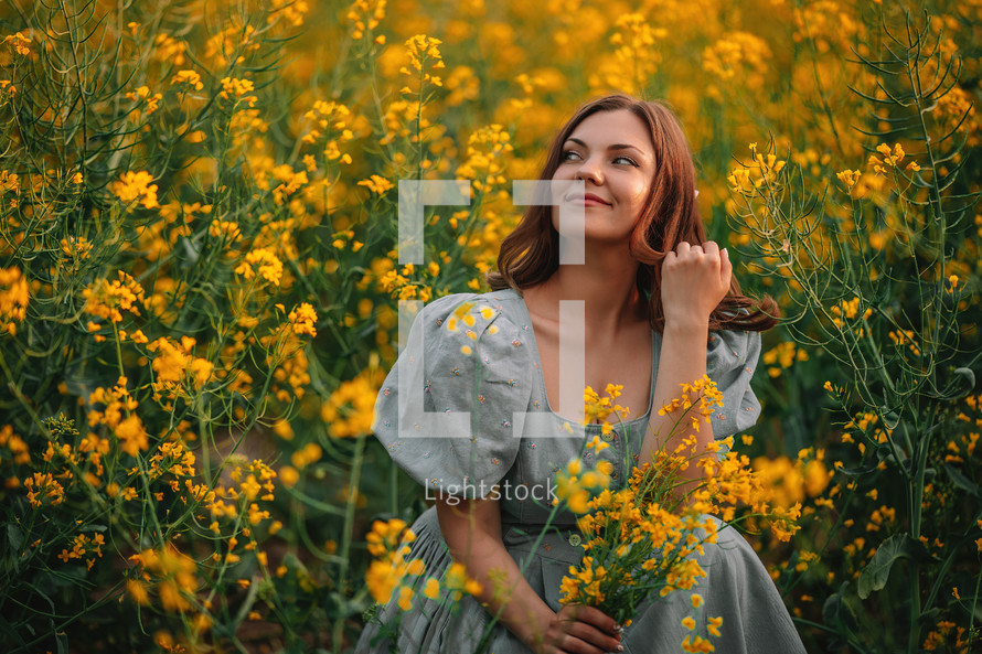 Portrait of attractive woman posing in blooming canola flowers field. Elegant girl in retro dress with straw hat, countryside nature place. Rapeseed meadow, vintage outfit, spring season