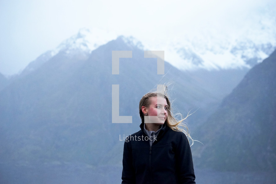 woman standing in front of snow capped mountains with hair blowing in the wind 
