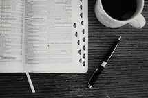 pen, open Bible, and coffee mug on a table 