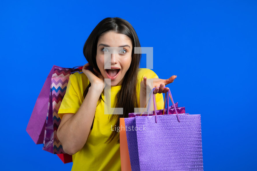 Excited woman with colorful paper bags after shopping on blue studio background. Concept of seasonal sale, purchases, spending money on gifts. High quality photo
