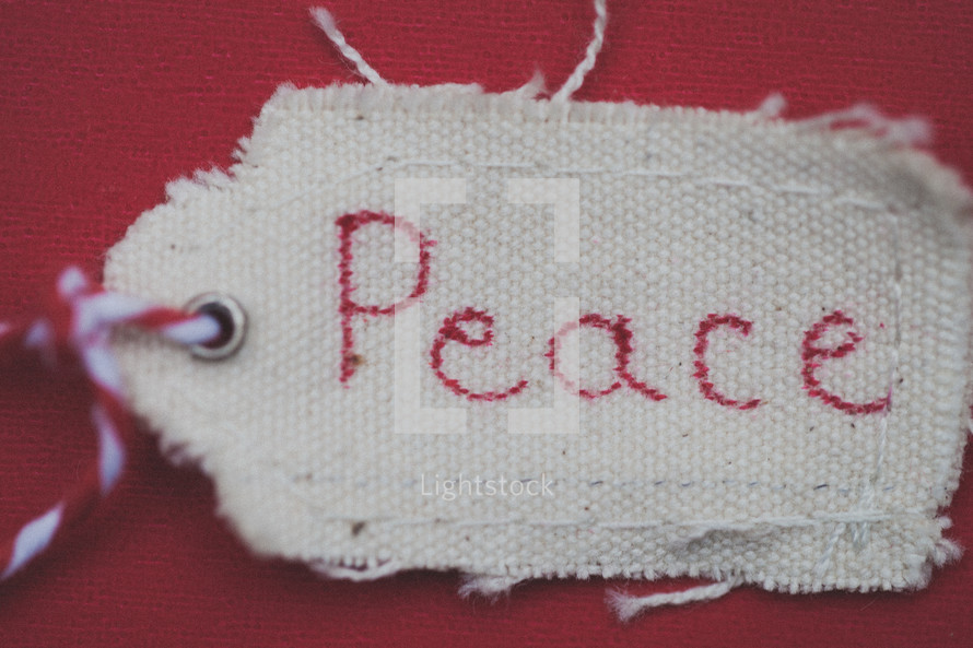 A Christmas gift tag reading "Peace," on a red background.