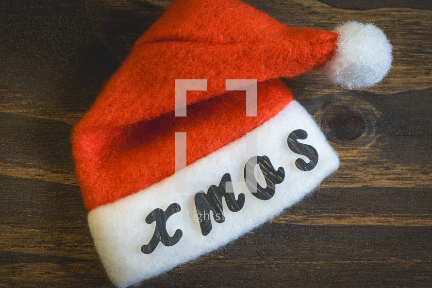 A little Santa hat with the letters Xmas on it. On a wooden background. background for Christmas.