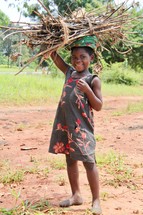 A little African girl carrying a bundle of sticks on her head 