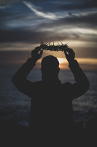 man holding up a crown of thorns at sunset 