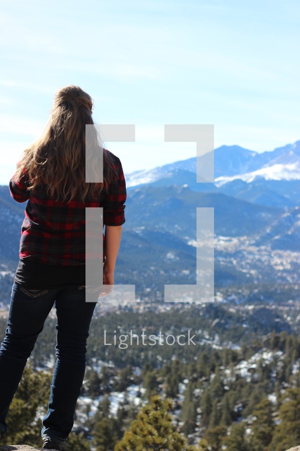 woman standing on a mountaintop looking out at the snowy landscape below