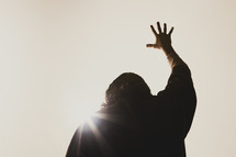Jesus' hand raised high in the air as the sun shines down on him