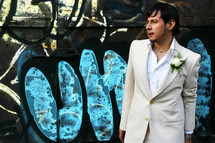 groom standing in front of a graffiti covered wall