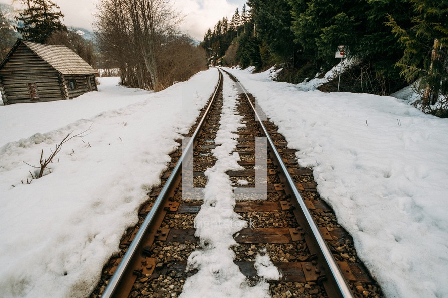 A railroad track by a log cabin in a snow covered landscape.