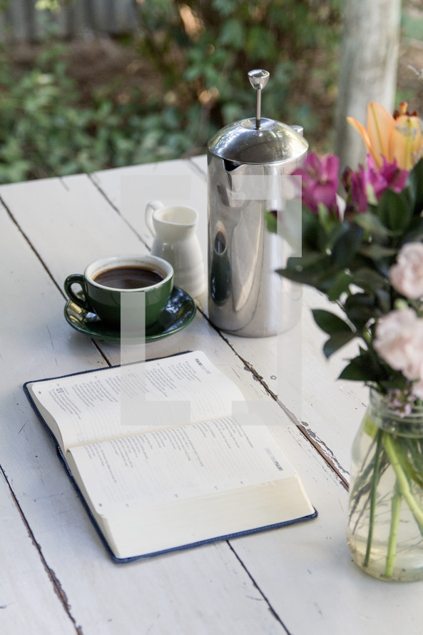 coffee, flower vase, and open Bible on a wood table 