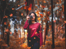a woman holding a camera in a forest with falling leaves 