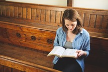 a woman reading alone sitting in the pews of a church 