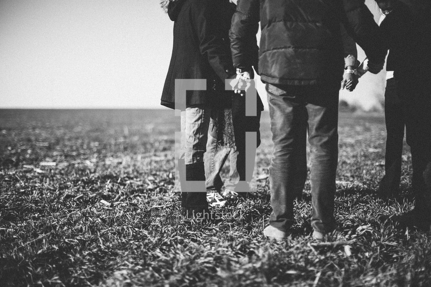 group holding hands in prayer in a field