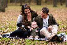 portrait of a young family sitting on a blanket in the grass 