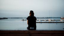 a girl sitting at a harbor looking out at the boats 