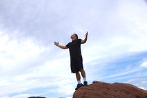 man standing on a red rock with arms raised