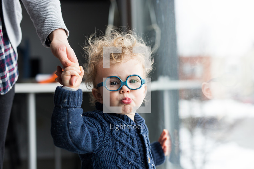 a toddler in glasses holding mom's hand 