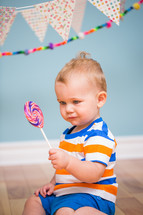 an infant boy holding a lollipop under a banner 