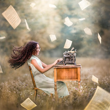 a girl typing in a field with papers flying everywhere 