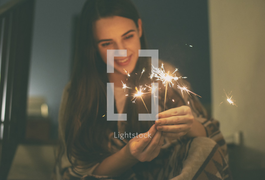 young woman sits on stairs holding sparklers 