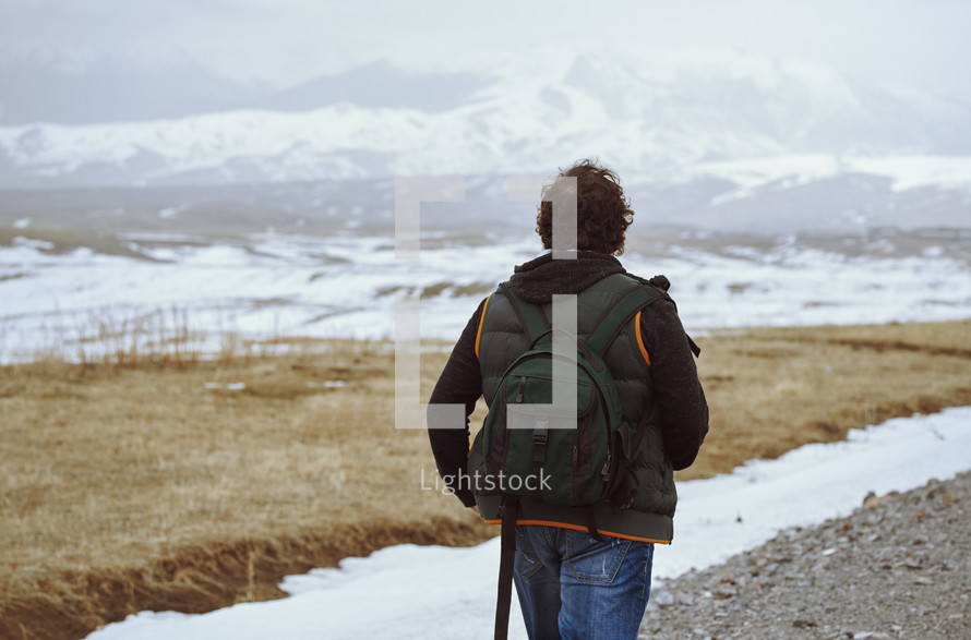 Man wearing backpack and looking at the winter mountains
