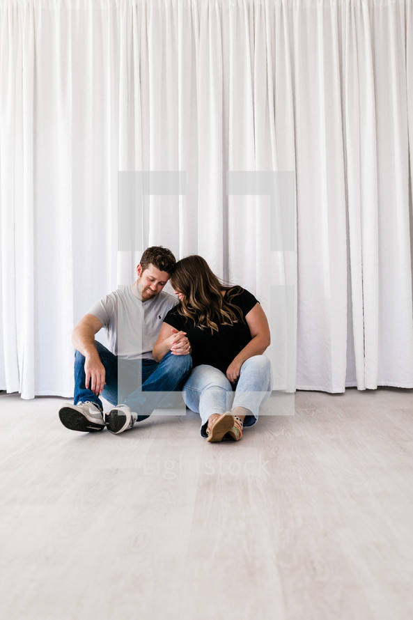 couple snuggling sitting on the floor of an empty house 