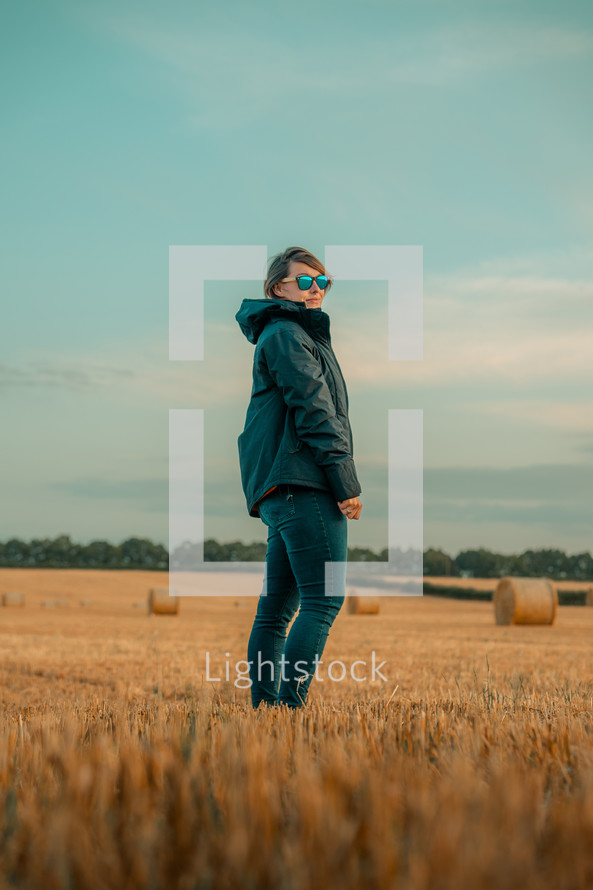 Woman wearing sunglasses hiking in a field, agricultural setting, harvest outdoors landscape scene
