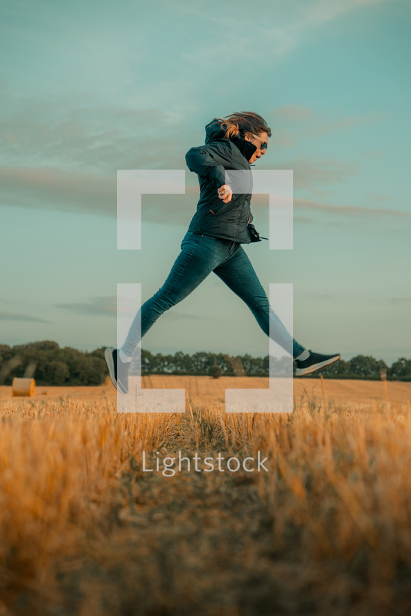 Jumping in a field, female woman jumps in the air outdoors, farm land agricultural setting, countryside