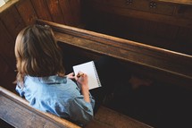 a woman sitting in a pew writing in a notebook 