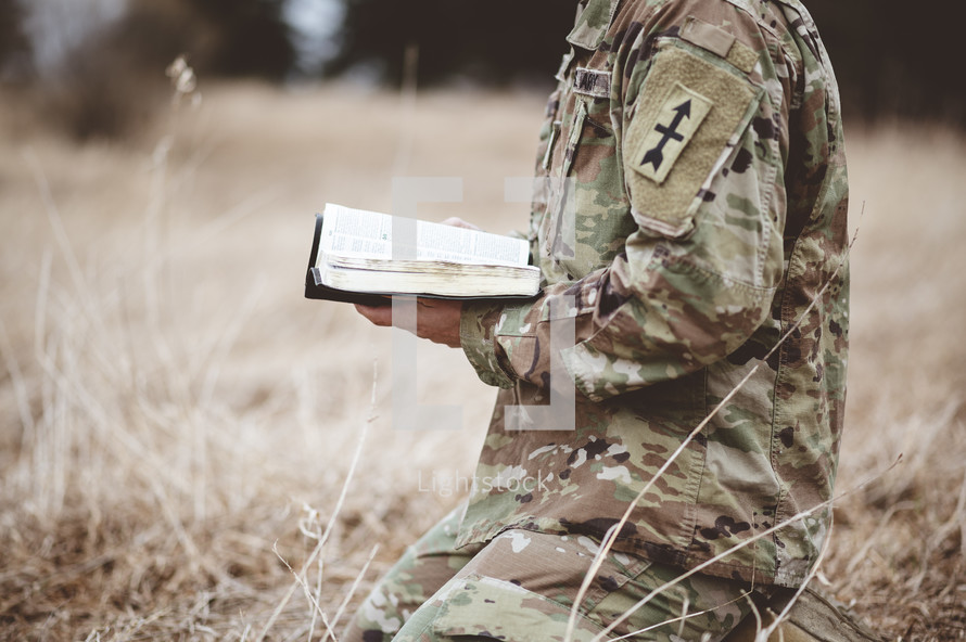 soldier kneeling in a field praying holding a Bible 